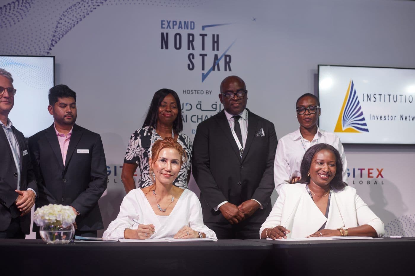 A signing ceremony in front of an exhibition backdrop bearing the network’s logo.